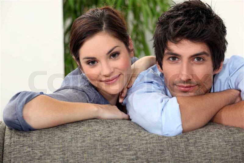 Smiling man and woman leaning on a couch, stock photo