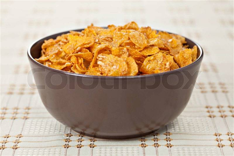 Brown ceramic bowl of crunchy nuts corn flakes for breakfast on the table with checkered tablecloth. Selective focus, stock photo