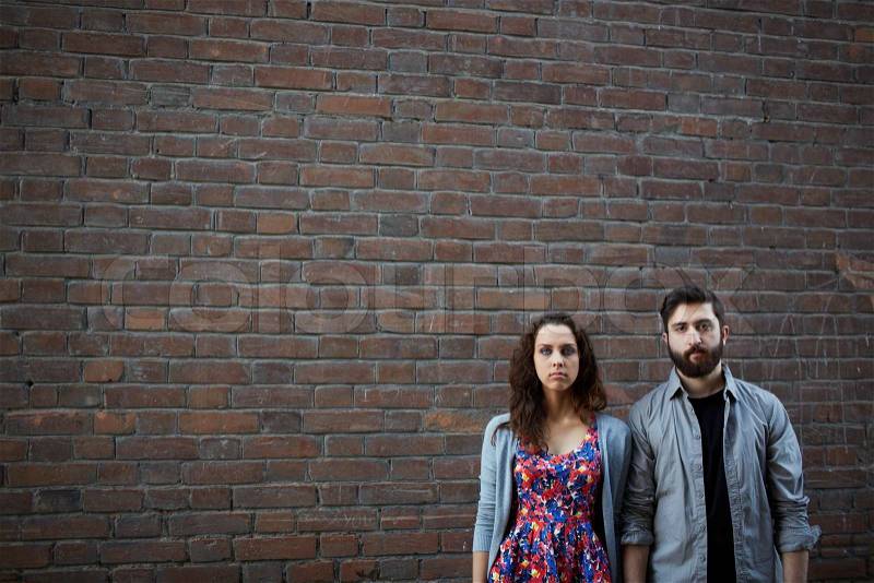 Portrait of serious couple standing by the brick wall, stock photo