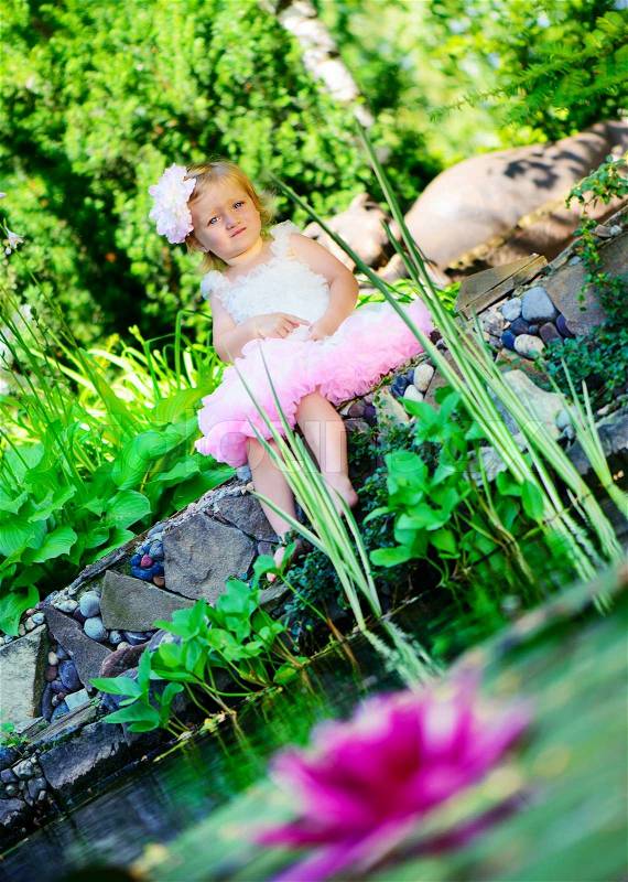 Cute little girl in ballerina tutu sitting at pond, stock photo