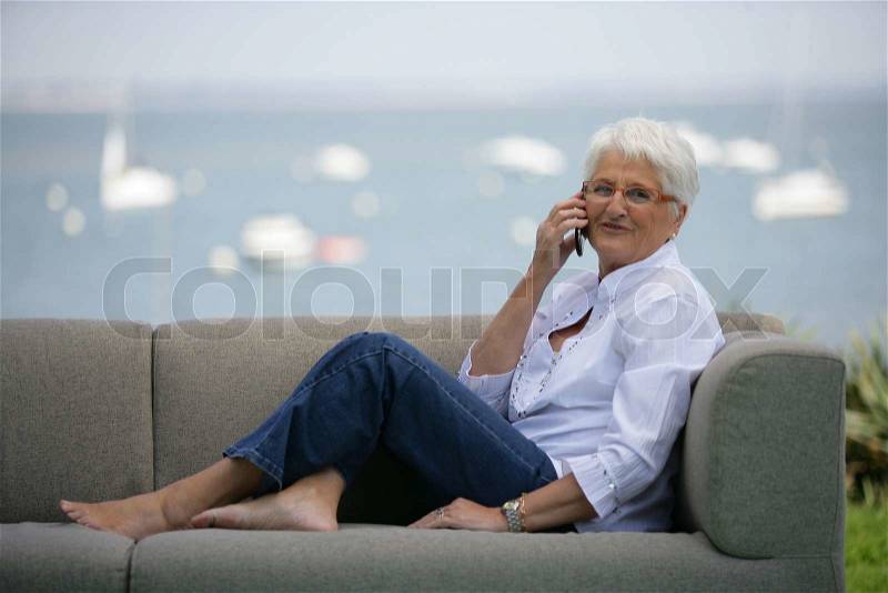 Elderly woman sat making a call on outdoor sofa, stock photo