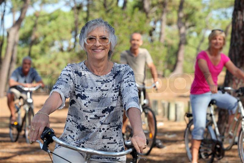 A 65 years old woman in first plan and three other people doing bike in the forest, stock photo