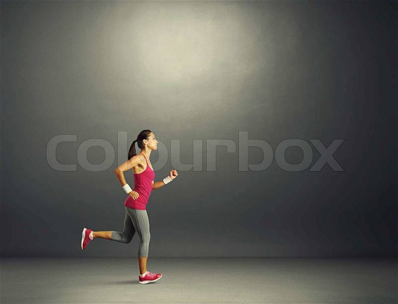 Young beautiful sportswoman running in the dark room, stock photo