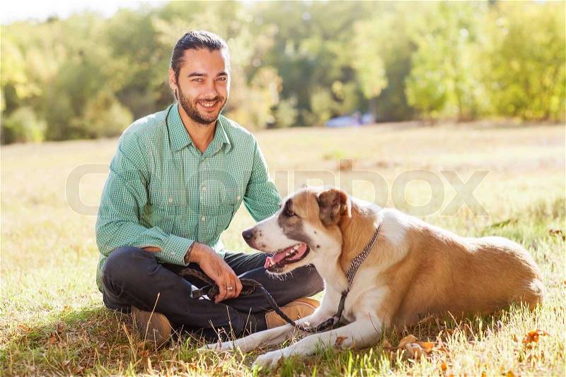 Man and central Asian shepherd walk in the park. He keeps the dog on the leash, stock photo