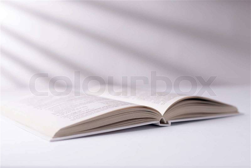 Open white hardcover book lying on a white surface in a shaft of sunlight with a radiating shadow pattern, low angle view, stock photo