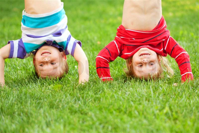 Happy children standing upside down on the grass. Fun kid\'s holiday, stock photo