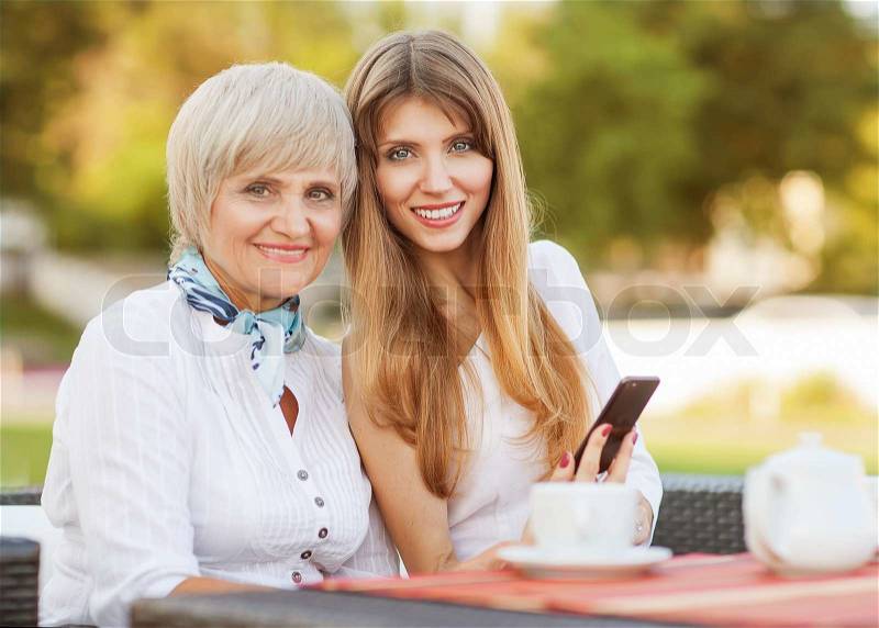 Adult mother and daughter drinking tea or coffee and talking outdoors, stock photo