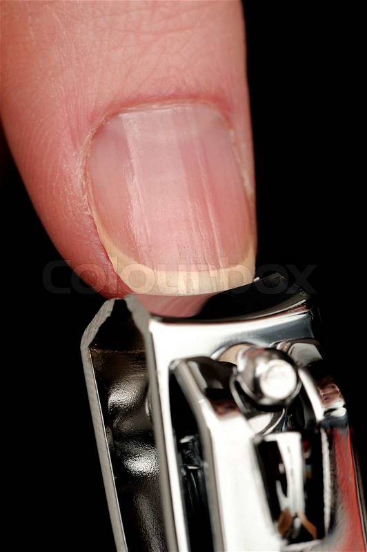 A close-up of a thumb nail being cut with a nail clipper against a black background, stock photo