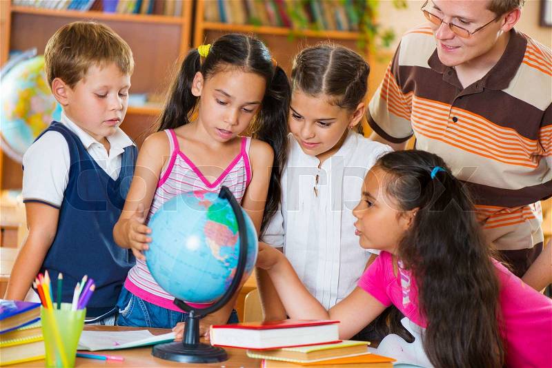 Portrait of pupils looking at globe with their teacher during geography lesson , stock photo