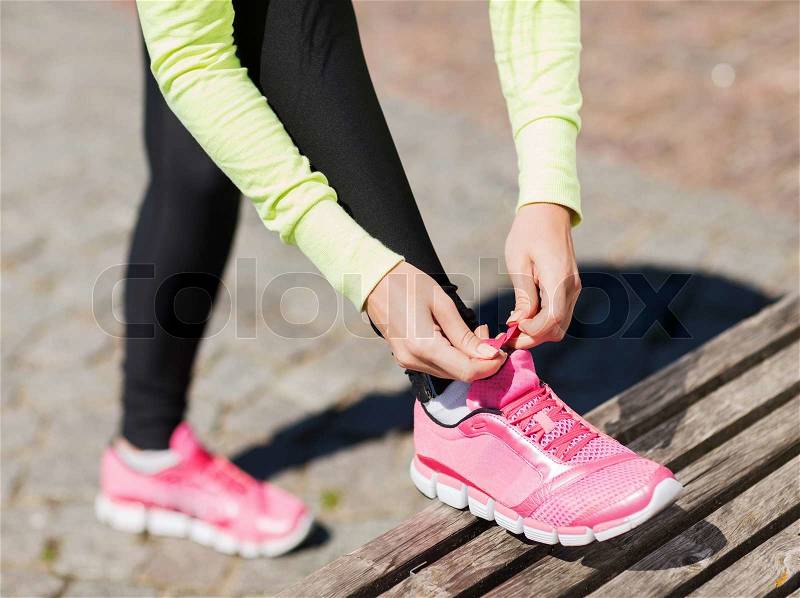 Sport, fitness, exercise and lifestyle concept - runner woman lacing trainers shoes, stock photo