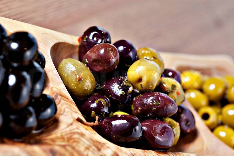 Variety of green, black and mixed marinated olives in olive tree dish on wooden table. Selective focus, stock photo
