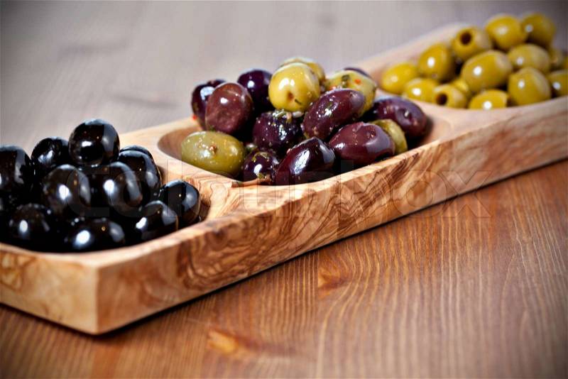 Variety of green, black and mixed marinated olives in olive tree dish on wooden table. Selective focus, stock photo