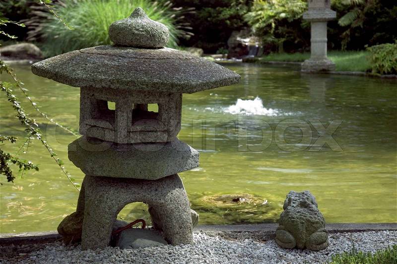 Beautiful weather worn stone pagoda and frog sitting next to a Japanese water garden. Shallow depth of field with Pagoda and frog in focus, blurred waterfall in background. , stock photo