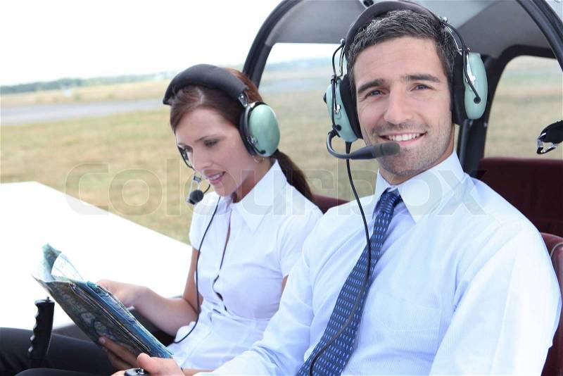 Smiling man sitting in the cockpit of a light aircraft as his partner consults a mapbook, stock photo