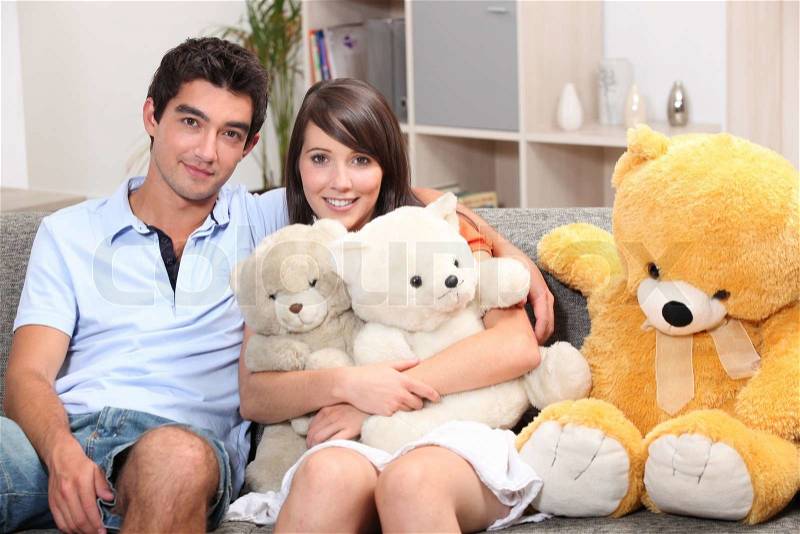 Couple sat on couch with cuddly toys, stock photo
