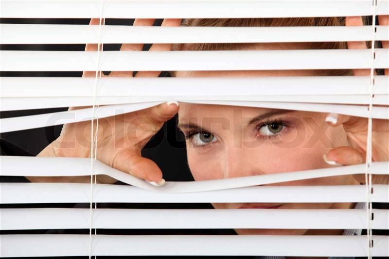 Woman peering through blinds, stock photo