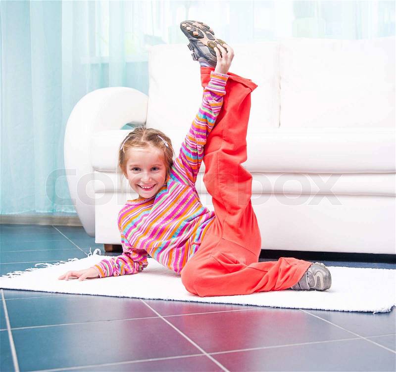 Pretty little girl playing sports at home in front of a white sofa, stock photo