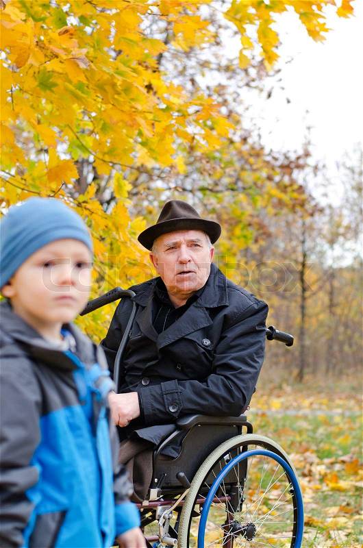 Disabled grandfather in a wheelchair and grandchild in the forest during autumn, stock photo