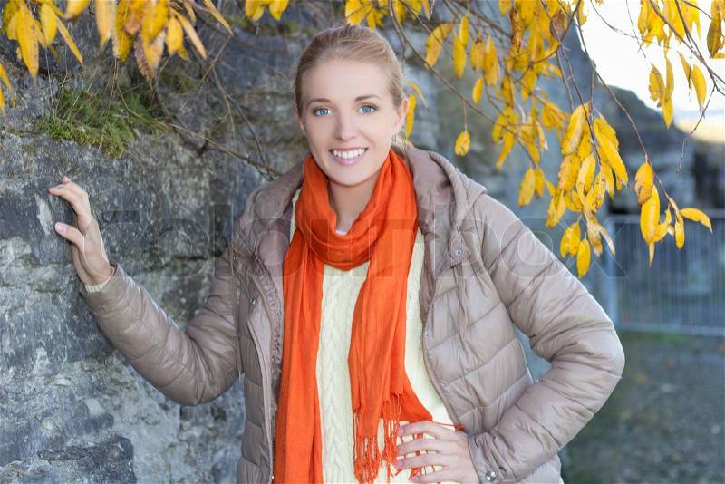 Young woman in warm clothes posing against stone wall, stock photo