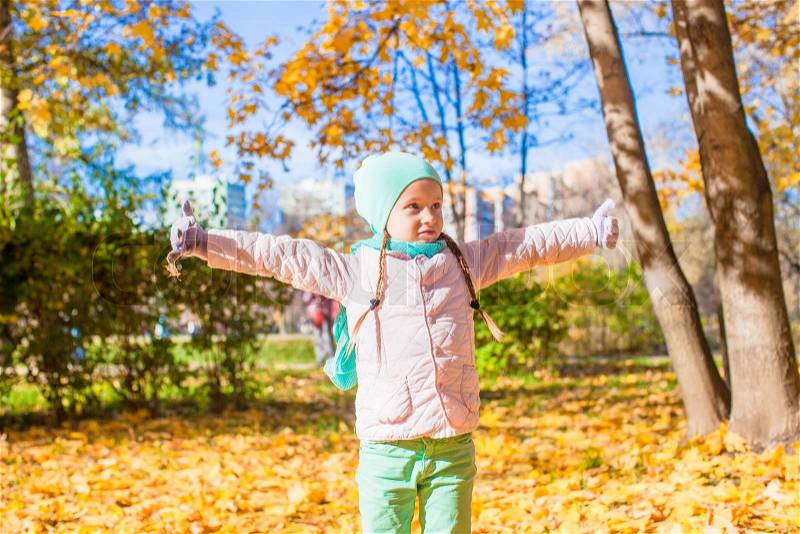 Little funny girl throws autumn leaves in the park on a sunny fall day, stock photo
