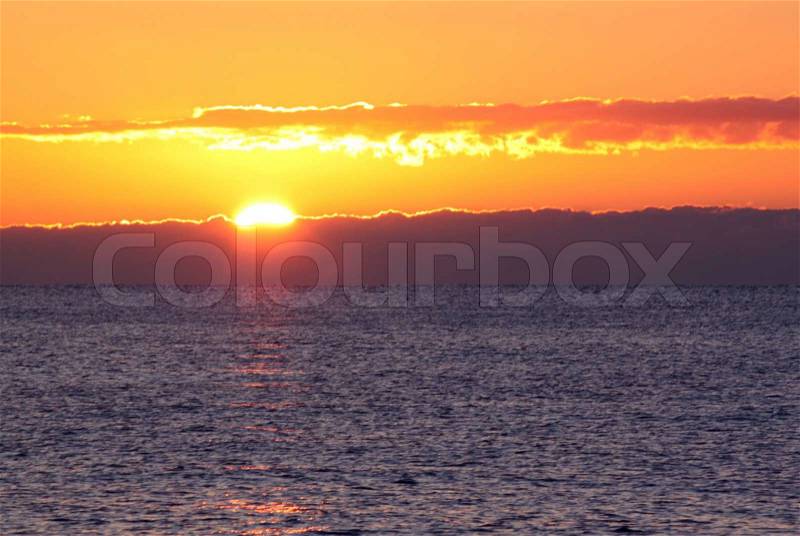 Sun rising behind sea and clouds, stock photo