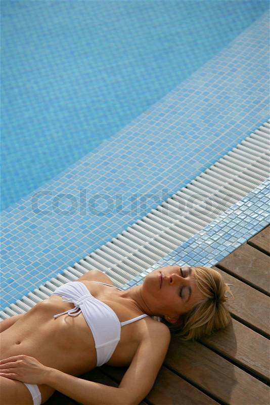 Blond woman resting next to swimming pool, stock photo