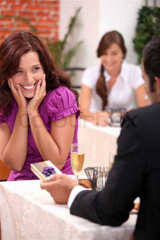 Man giving gift to woman in restaurant, stock photo