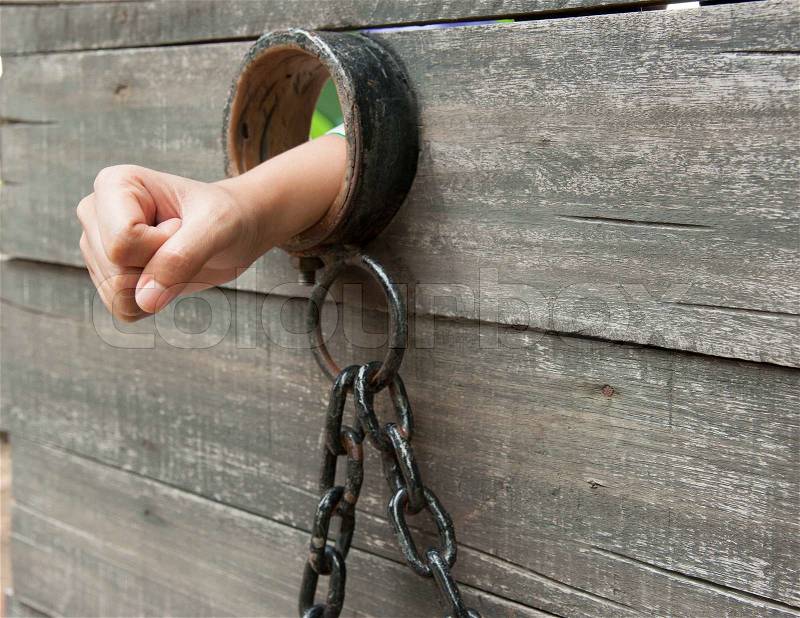 Locked Up hand is shackled to a vintage prison cell door with a ball and chain, stock photo