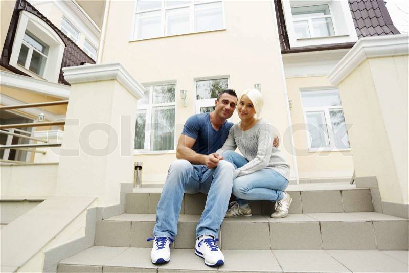 Happy couple sitting on the stairs in front of their house, stock photo