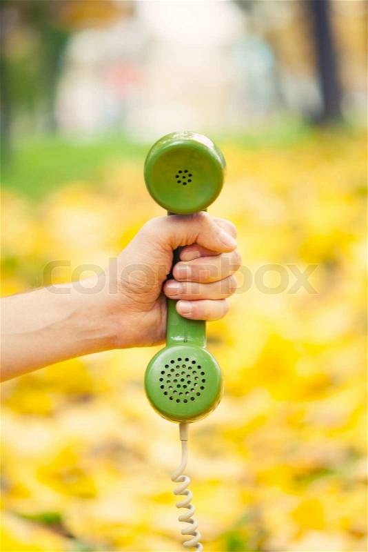 Hand holding vintage phone receiver in autumn park, stock photo