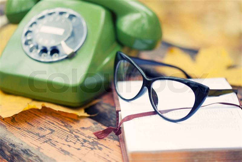 Green vintage phone, book and glasses on bench in autumn park, stock photo