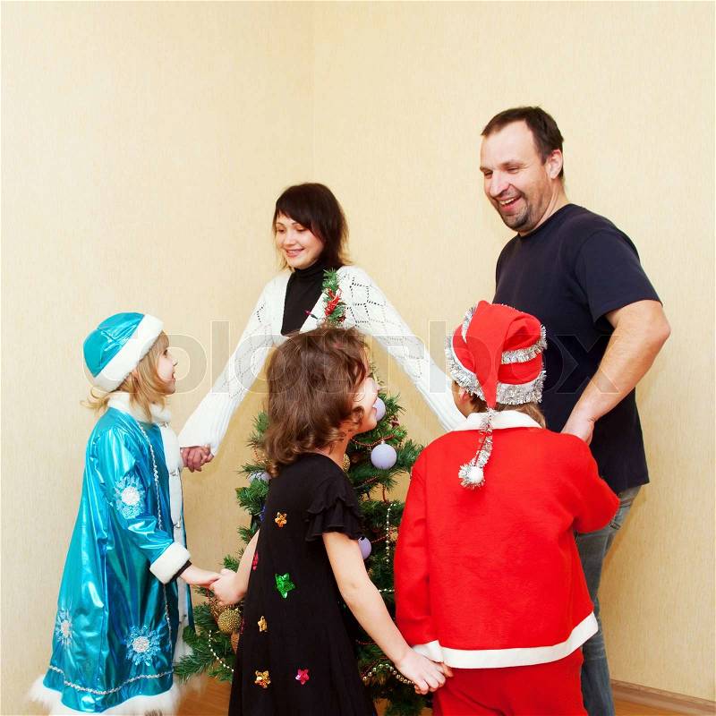 Family wearing in carnival costumes dancing around the Christmas tree. Holiday concept, stock photo