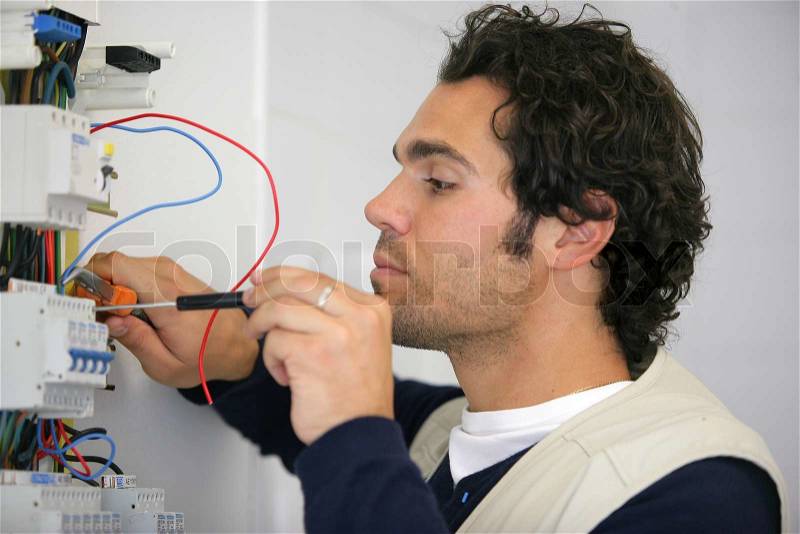 Trained electrician repairing fuse box, stock photo