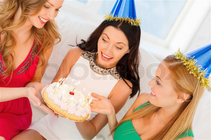 Celebration, food, friends, bachelorette party, birthday concept - three smiling women wearing blue hats holding cake with candles, stock photo