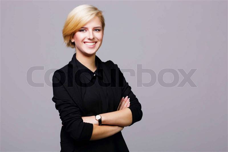 Confident beautiful young woman with arms folded on gray background, stock photo
