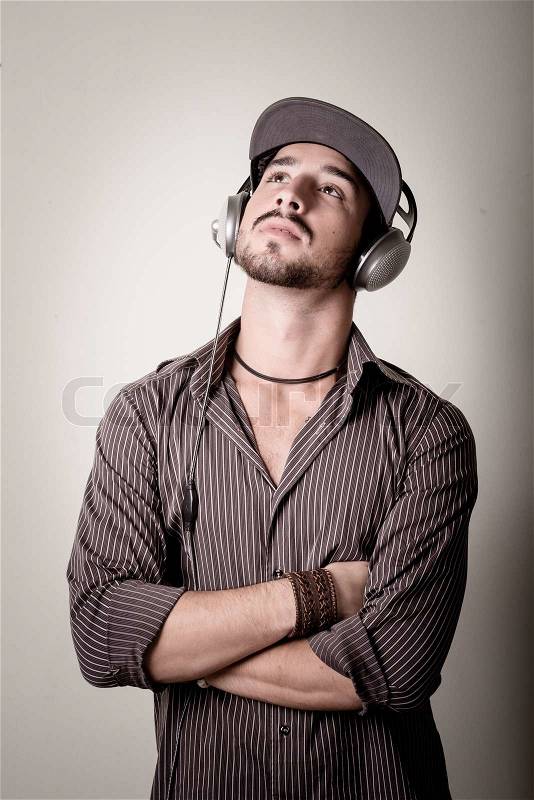 Young stylish man listening to music on gray background, stock photo
