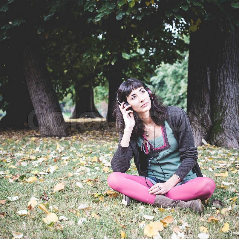 Young beautiful woman listening to music at the park in autumn, stock photo