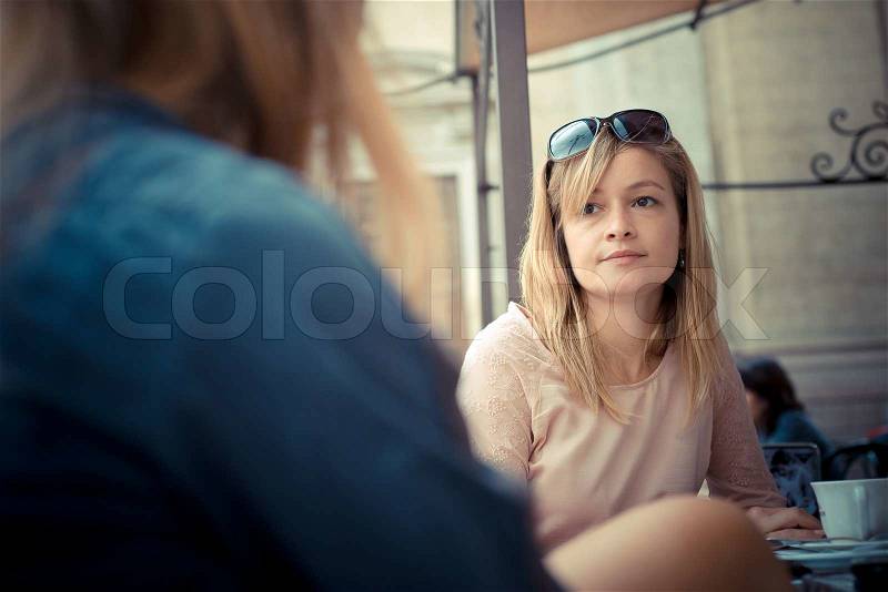 Two beautiful blonde women talking at the bar in the city, stock photo