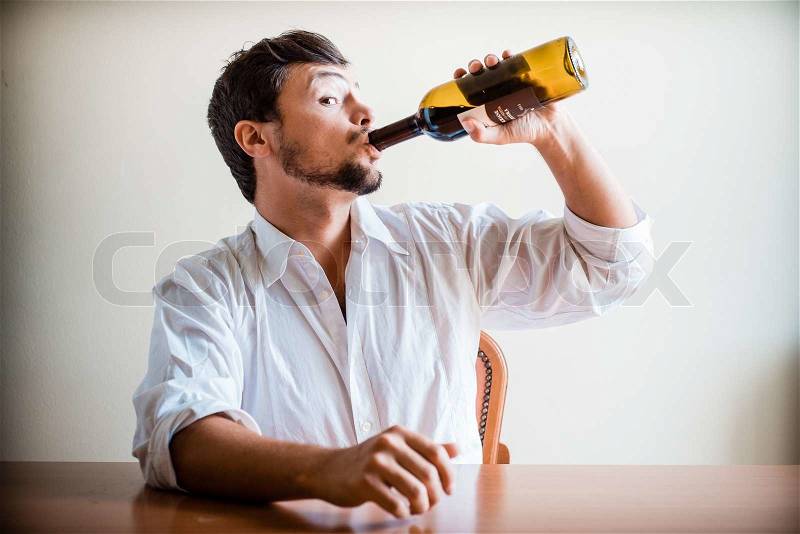 Drunk young stylish man with white shirt behind a table, stock photo