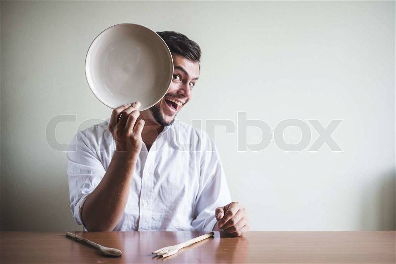 Young stylish man with white shirt and dish in his face behind a table, stock photo