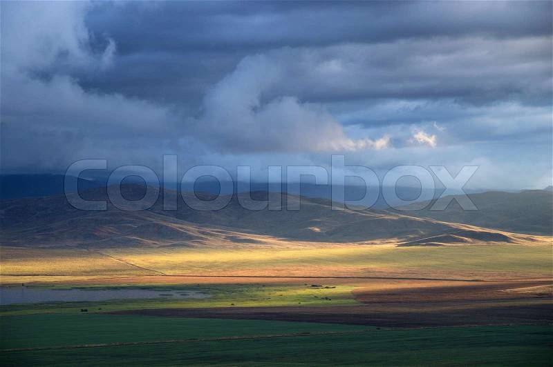 Storm sky and sun gaps on the fields and hills on the horizon, stock photo