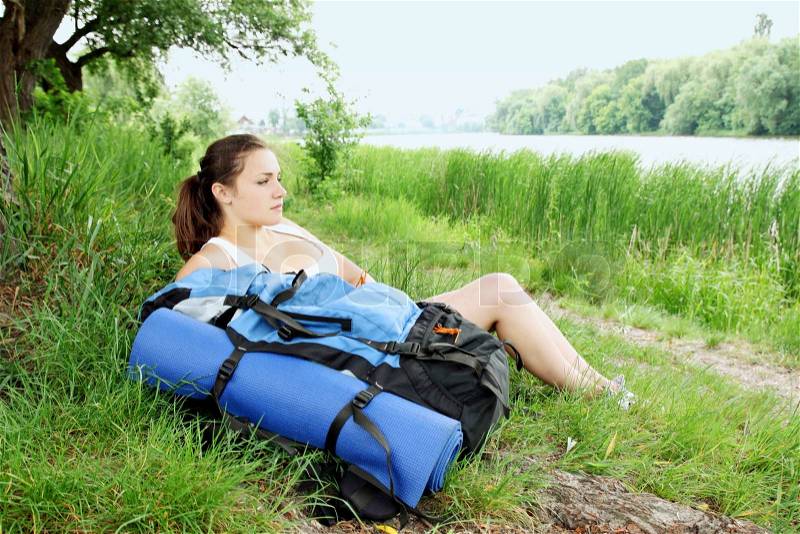 Woman with a backpack resting on the bank of the river, stock photo