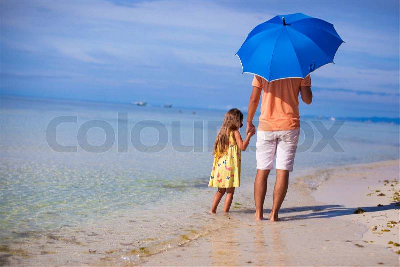 Young father and his little daughter walking under a blue umbrella on white sand beach, stock photo
