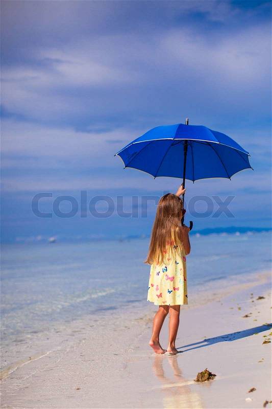 Little cute girl with big blue umbrella walking on a tropical beach, stock photo