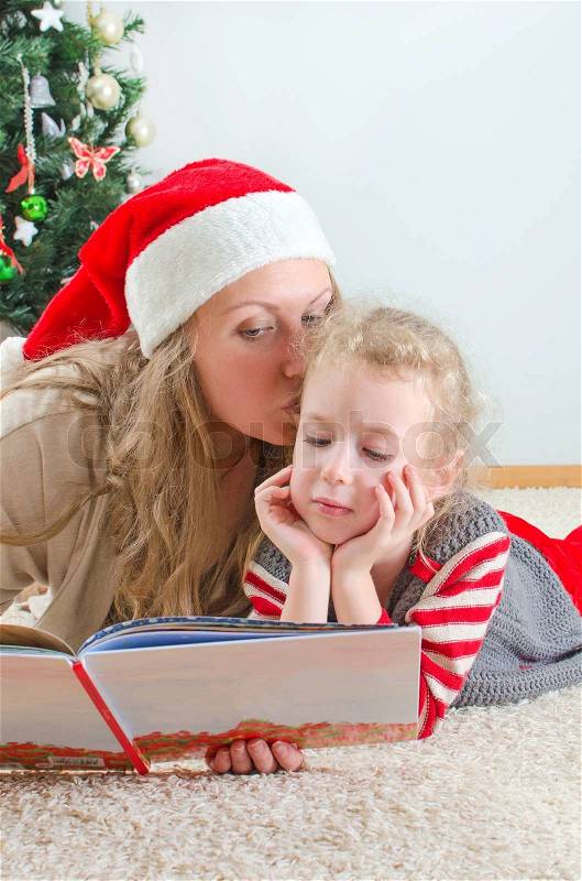 Little girl and her mom reading book at Christmas, stock photo