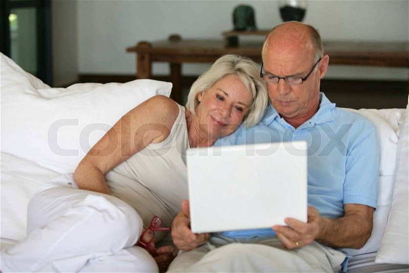 Middle-aged couple sat on sofa with laptop, stock photo