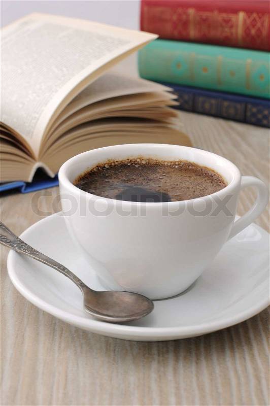 A cup of fragrant black coffee on the table against the background of an open book, stock photo