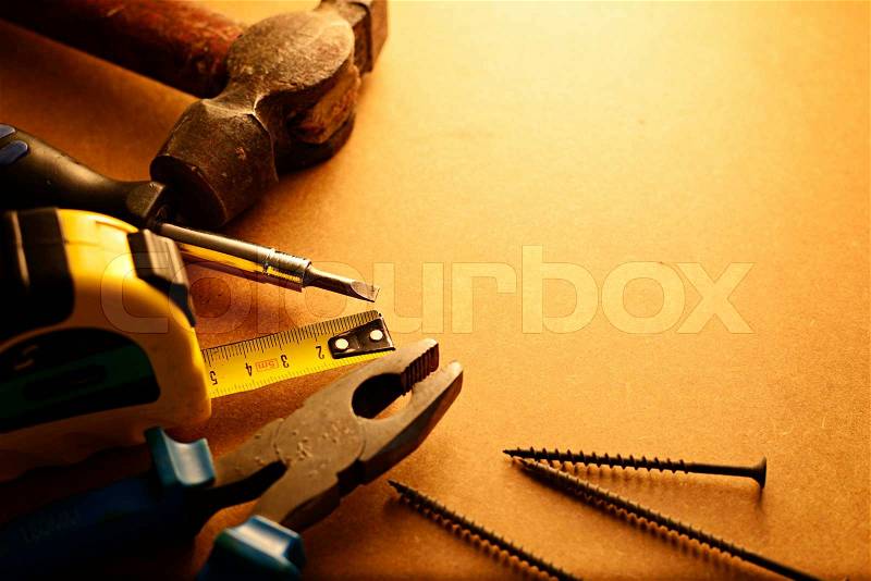 Home maintenance tool kit in a sepia toned image arranged in a semi circle on the border with a hammer, pliers, screwdriver, tape measure and nails surrounding copyspace, stock photo