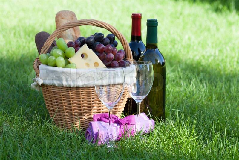 Outdoor picnic basket with bread, cheese and grape and wine bottles on lawn, stock photo