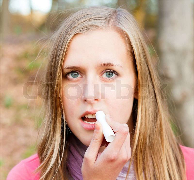 Young beautiful woman using lip balm to prevent dehydration during winter, stock photo